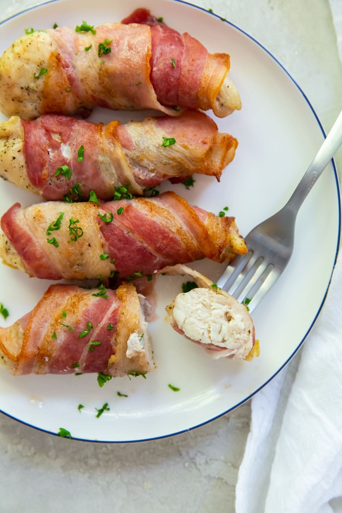 Bacon wrapped chicken tenders one piece cut with a fork in it.