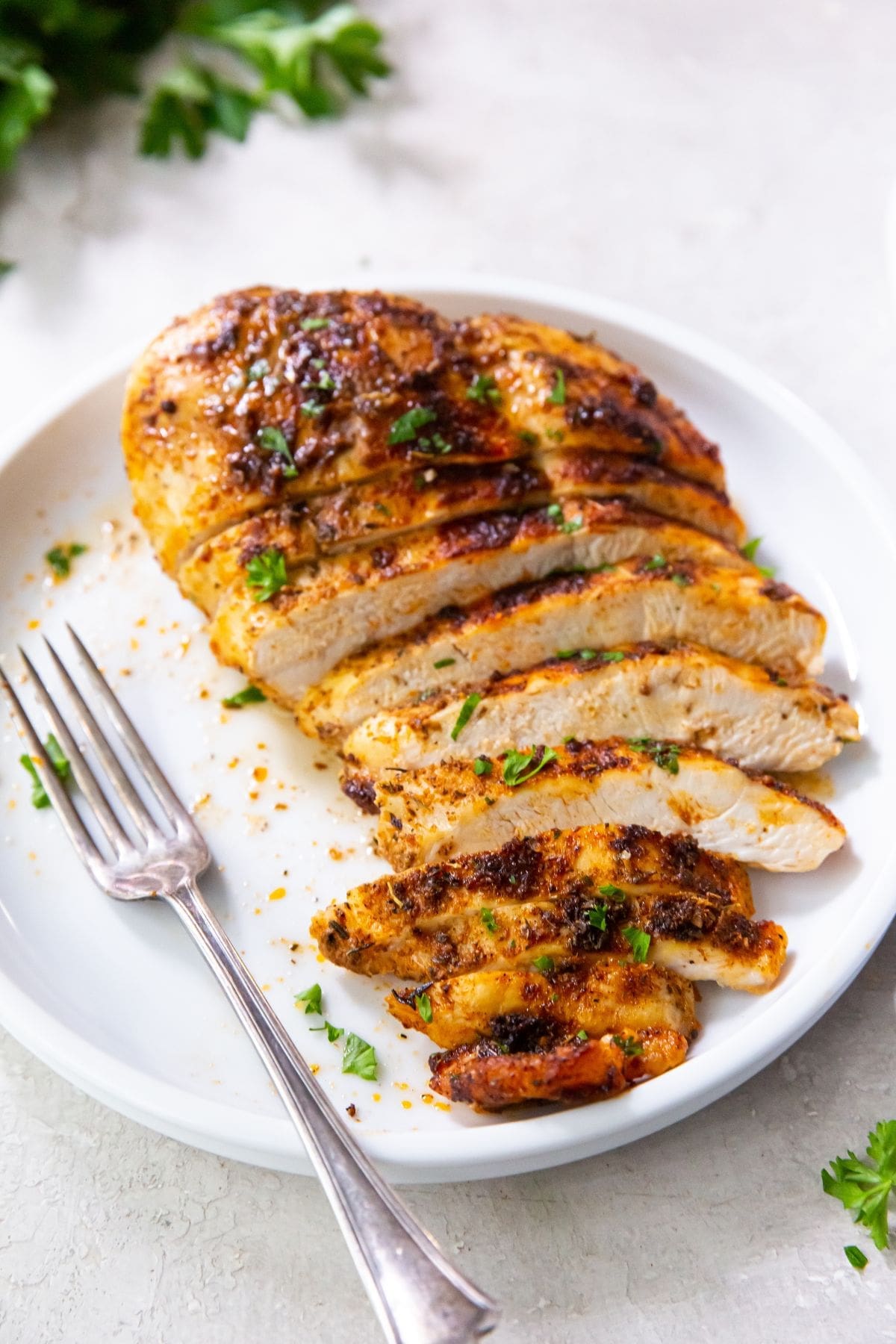 blackened chicken breast cut up on a white plate fork on plate