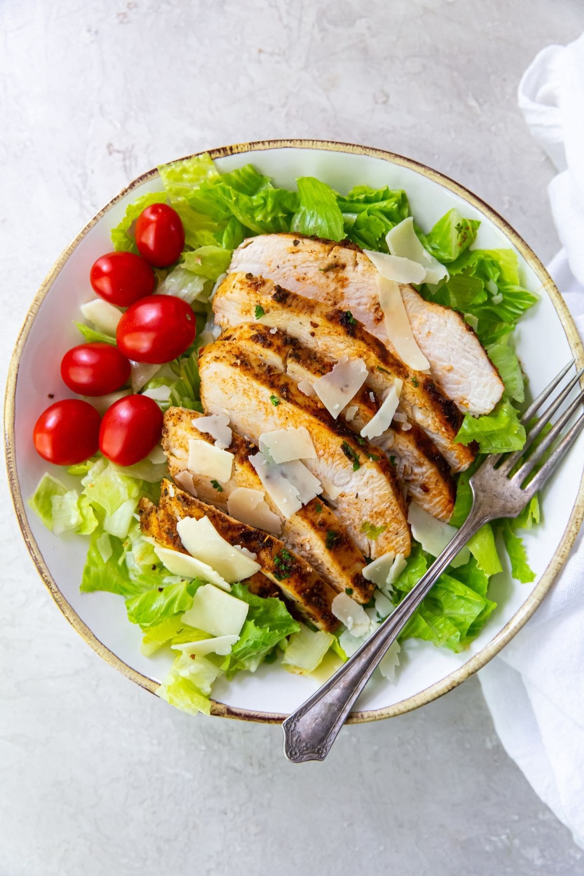 bowl with lettuce, tomato and parmesan cheese with sliced blacked chickened on top
