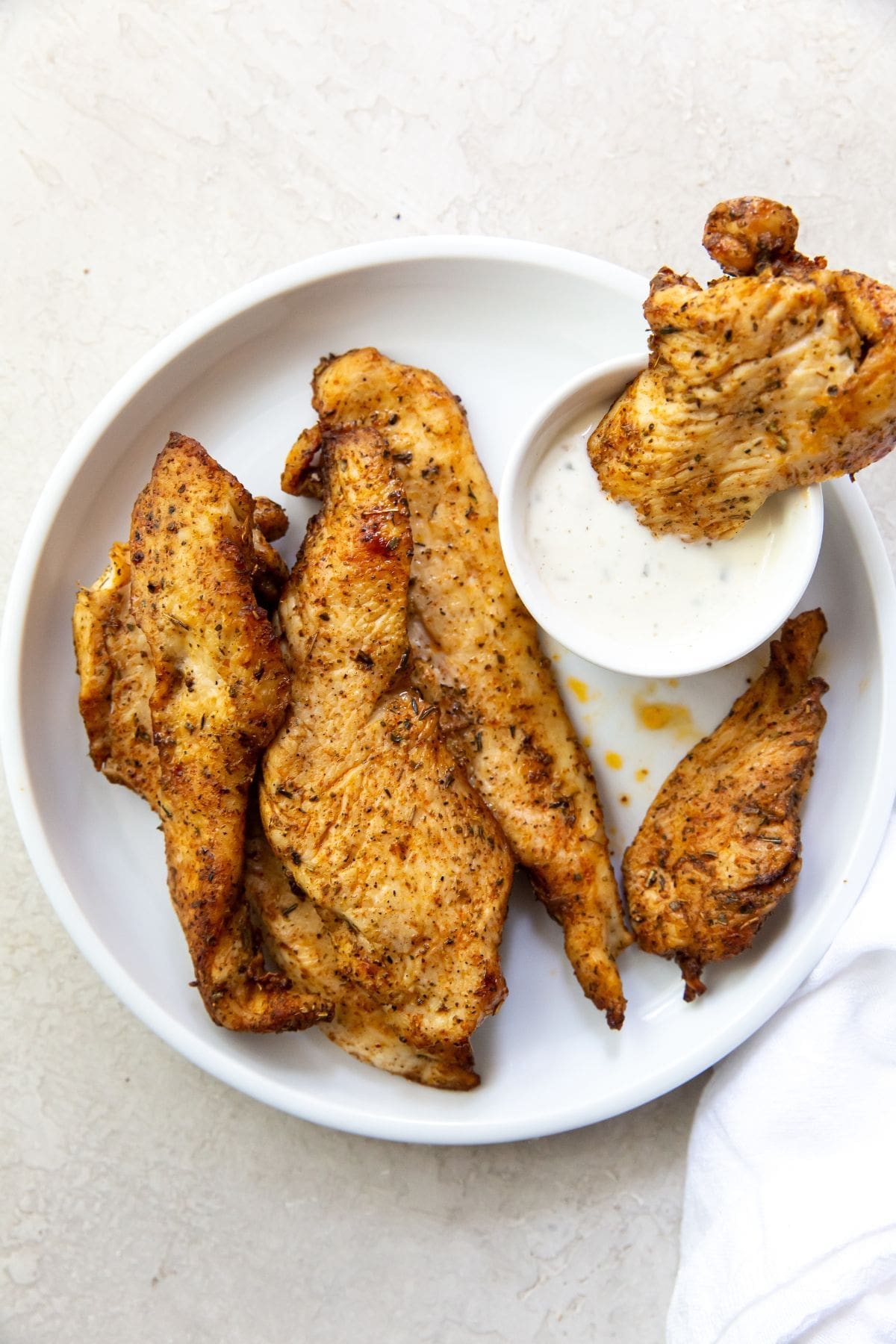 Gray background with white plate chicken breast tenders. One dipped into a side dish of ranch