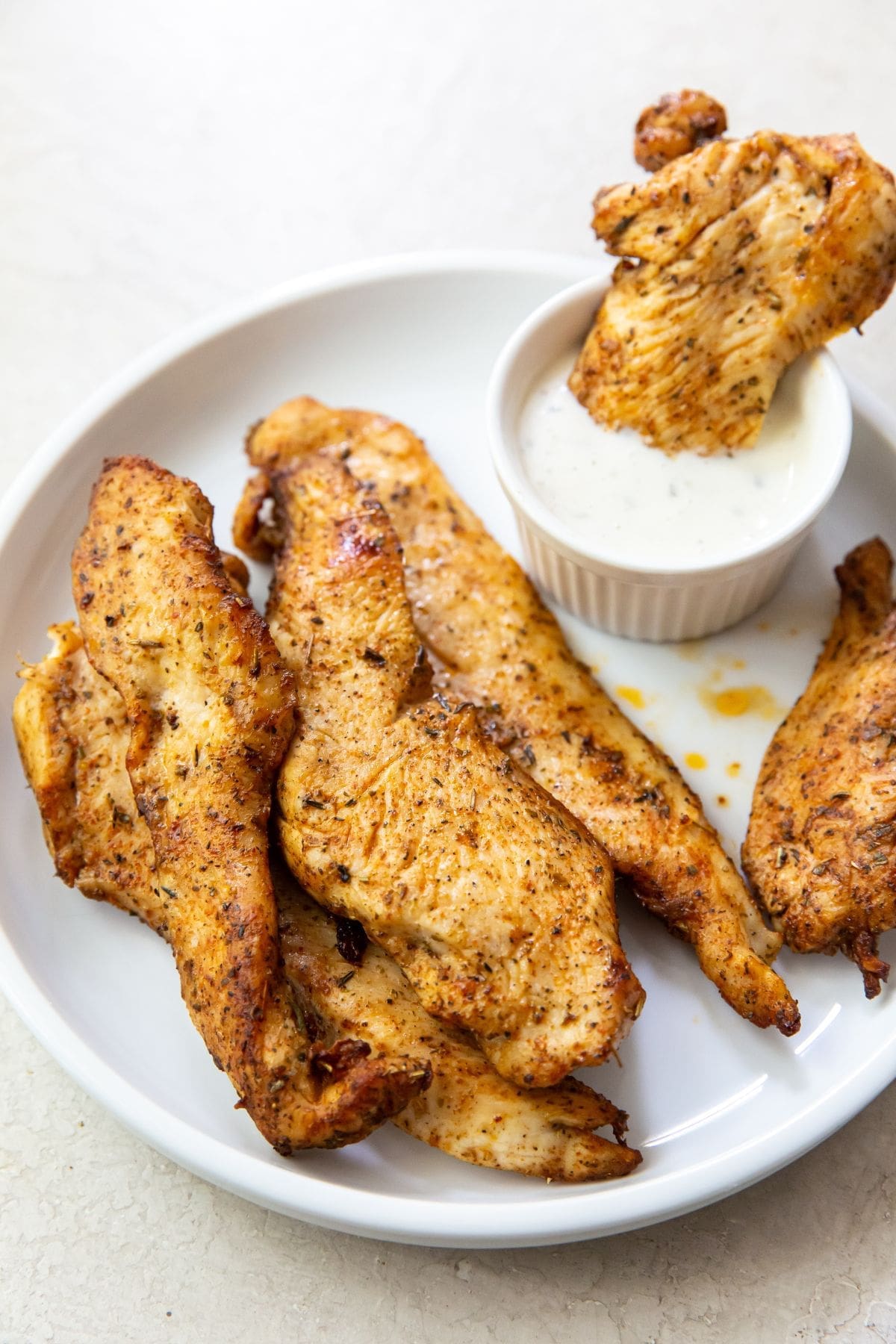 White plate with chicken breast strips with white side dish ranch inside