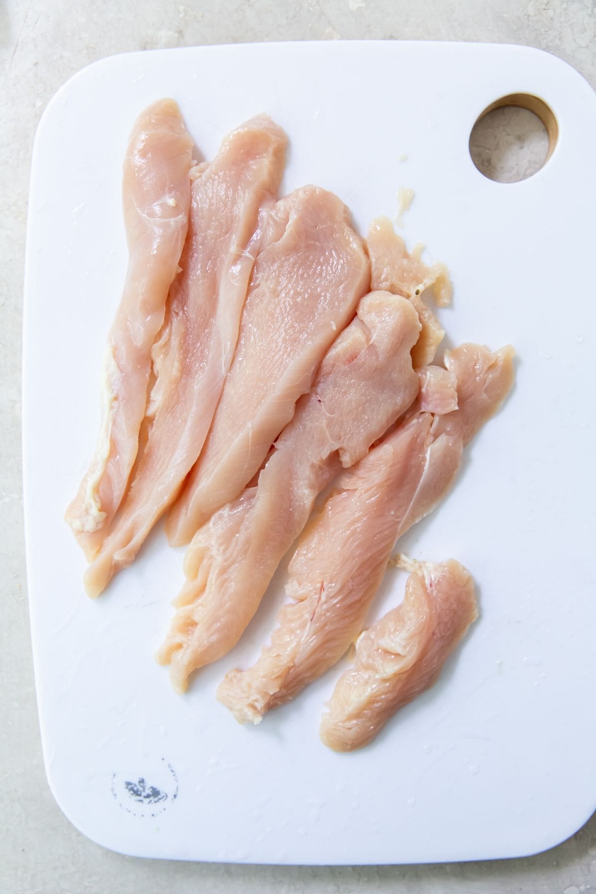 White cutting board with chicken breast cut up into strips