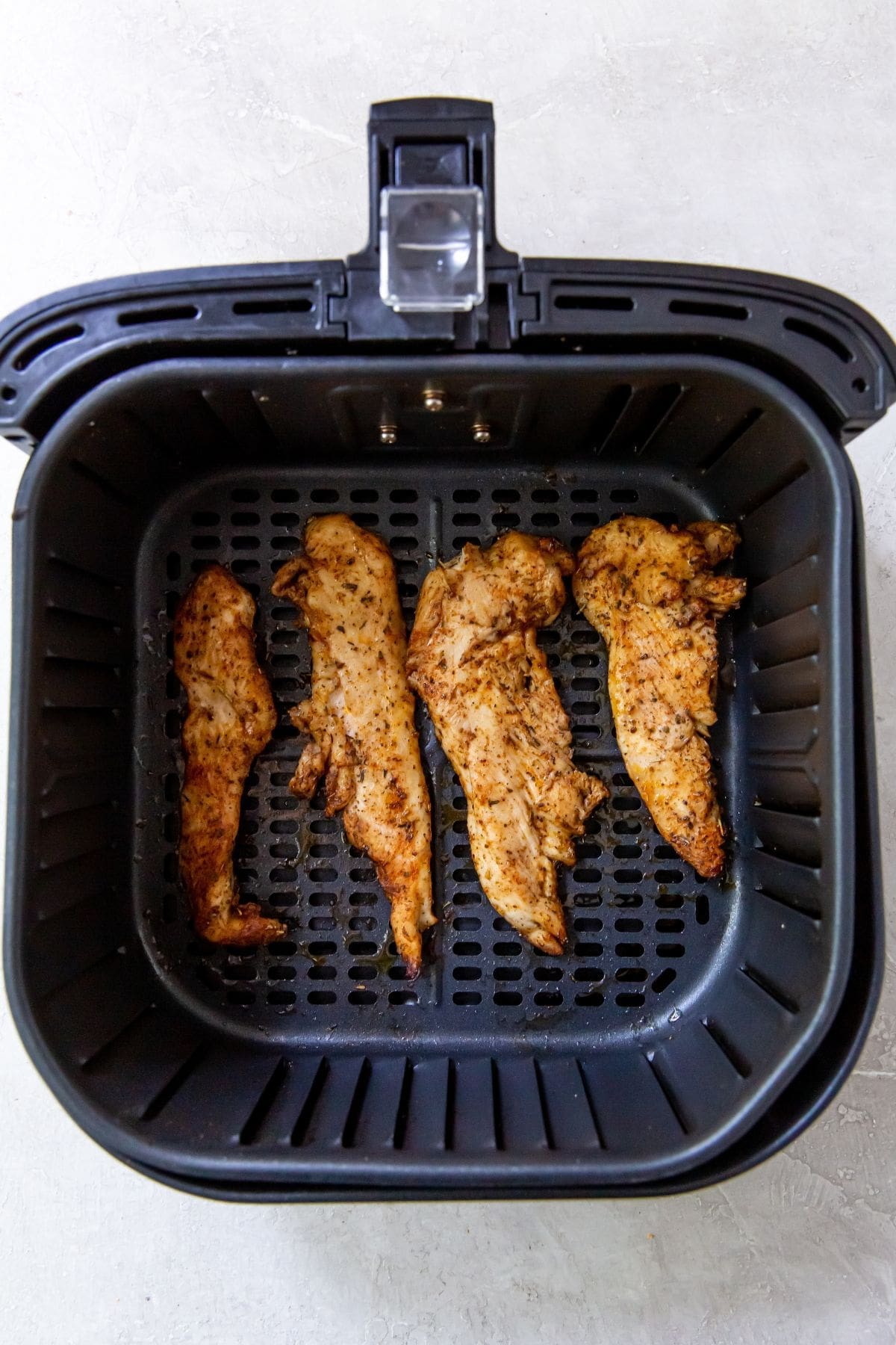 Black Air fryer with 4 cooked chicken breast strips