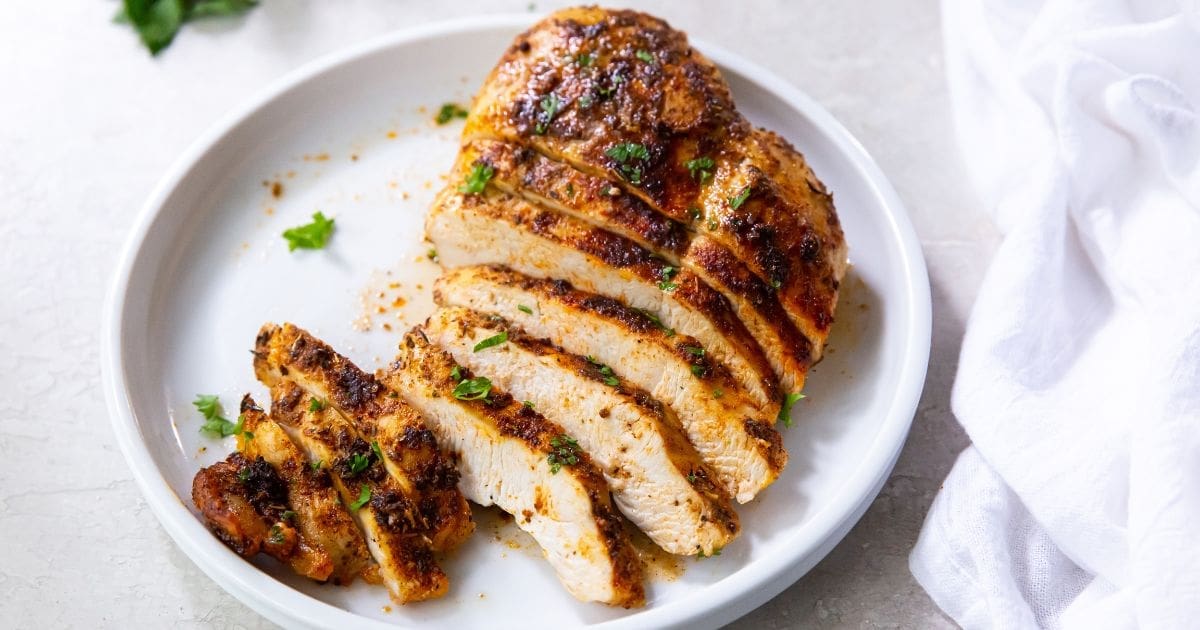 Air Fryer Blackened Chicken Breast on a white plate with parsley and a fork.