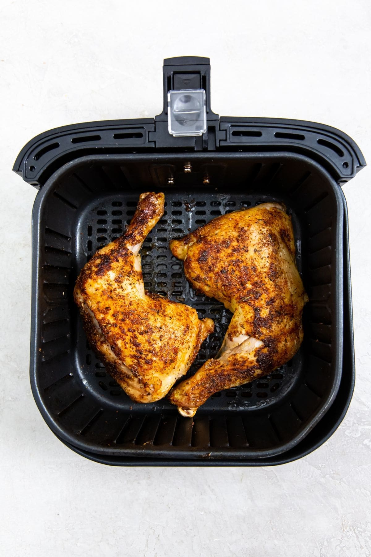 black air fryer basket with cooked leg quarters inside