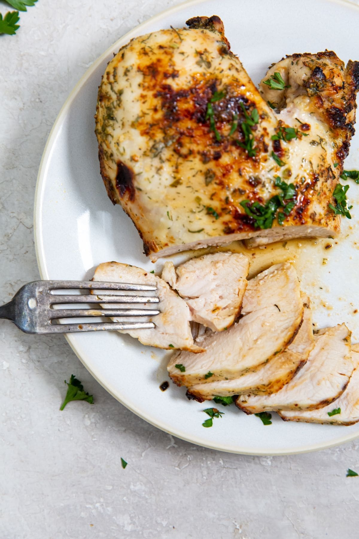 white plate with chicken breast on it parsley in the back. fork on the plate