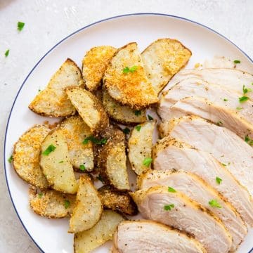 two plates with chicken breast and potatoes parsley in the background