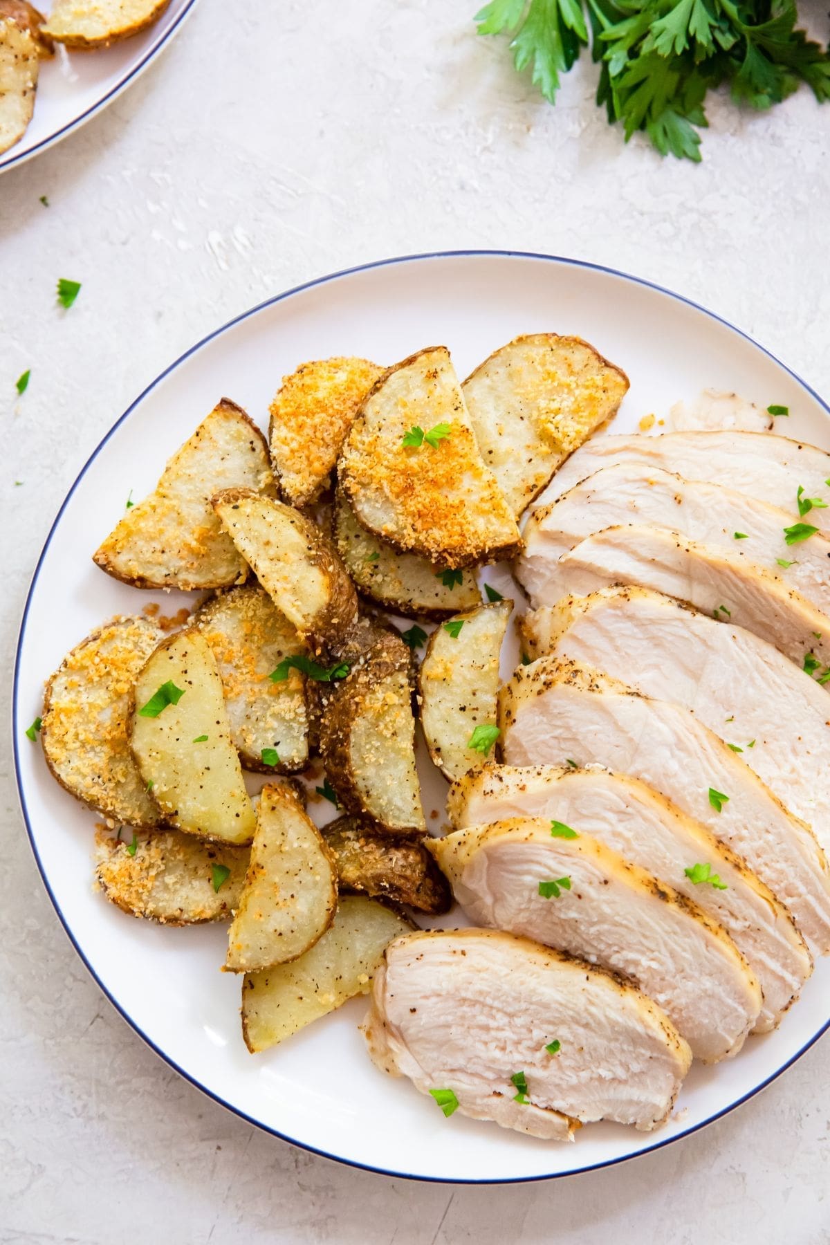 two plates with chicken breast and potatoes parsley in the back