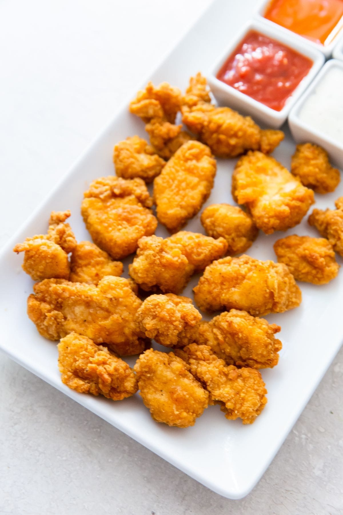 white plate with popcorn chicken on it buffalo, ketchup and ranch in the back
