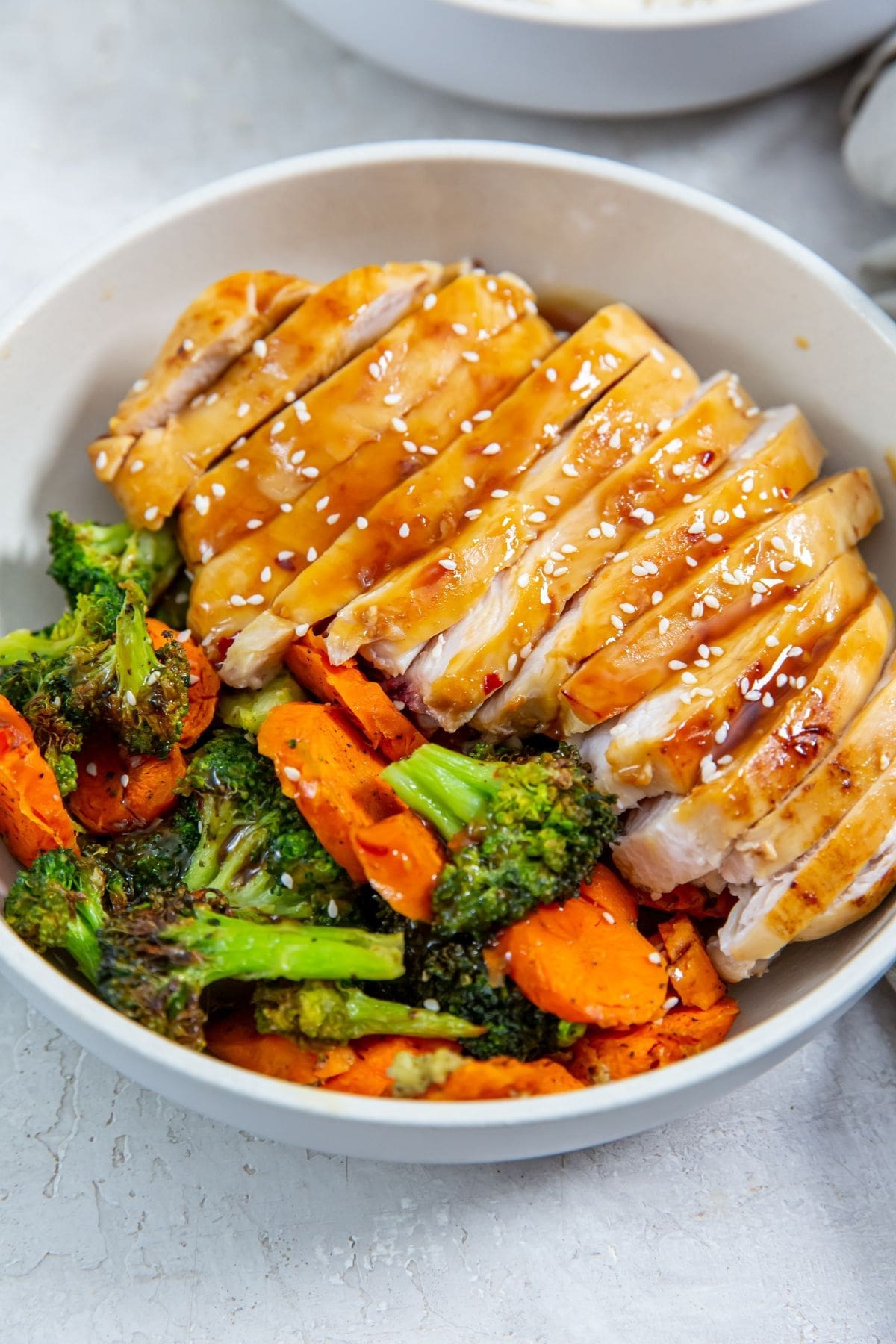 white bowl with chicken veggies and rice inside. gray towel next to it
