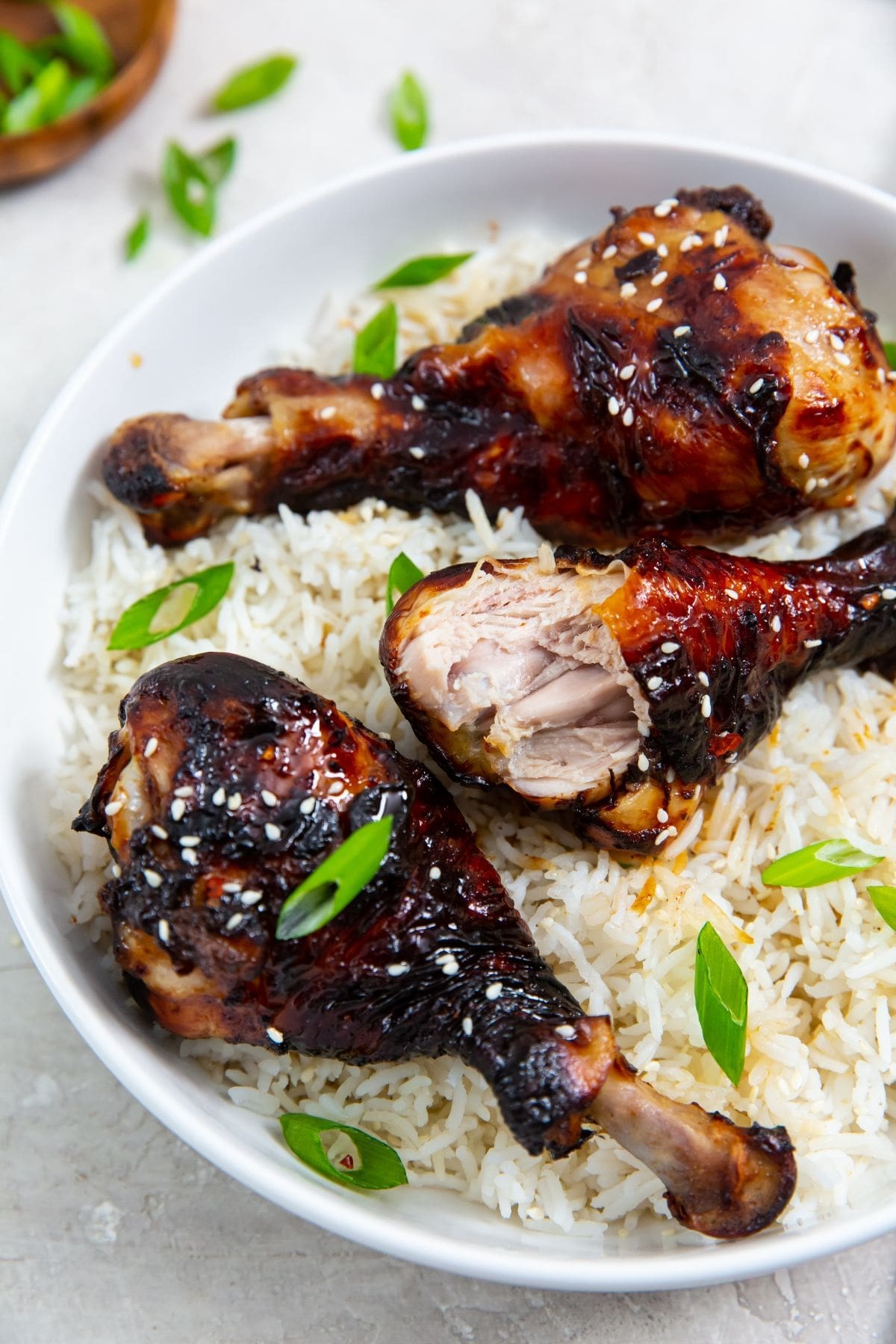 white bowl with rice and chicken legs inside. green onions in the back. Green towel next to bowl.