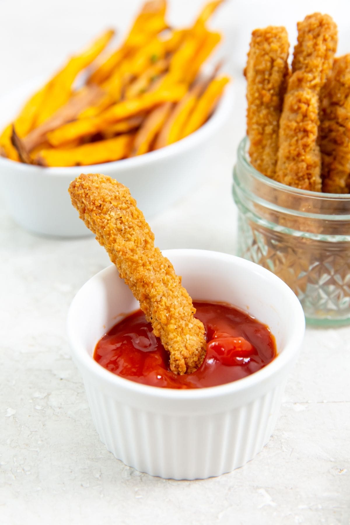 chicken fries dunk in ketchup. chicken fries and sweet potato fries in the background