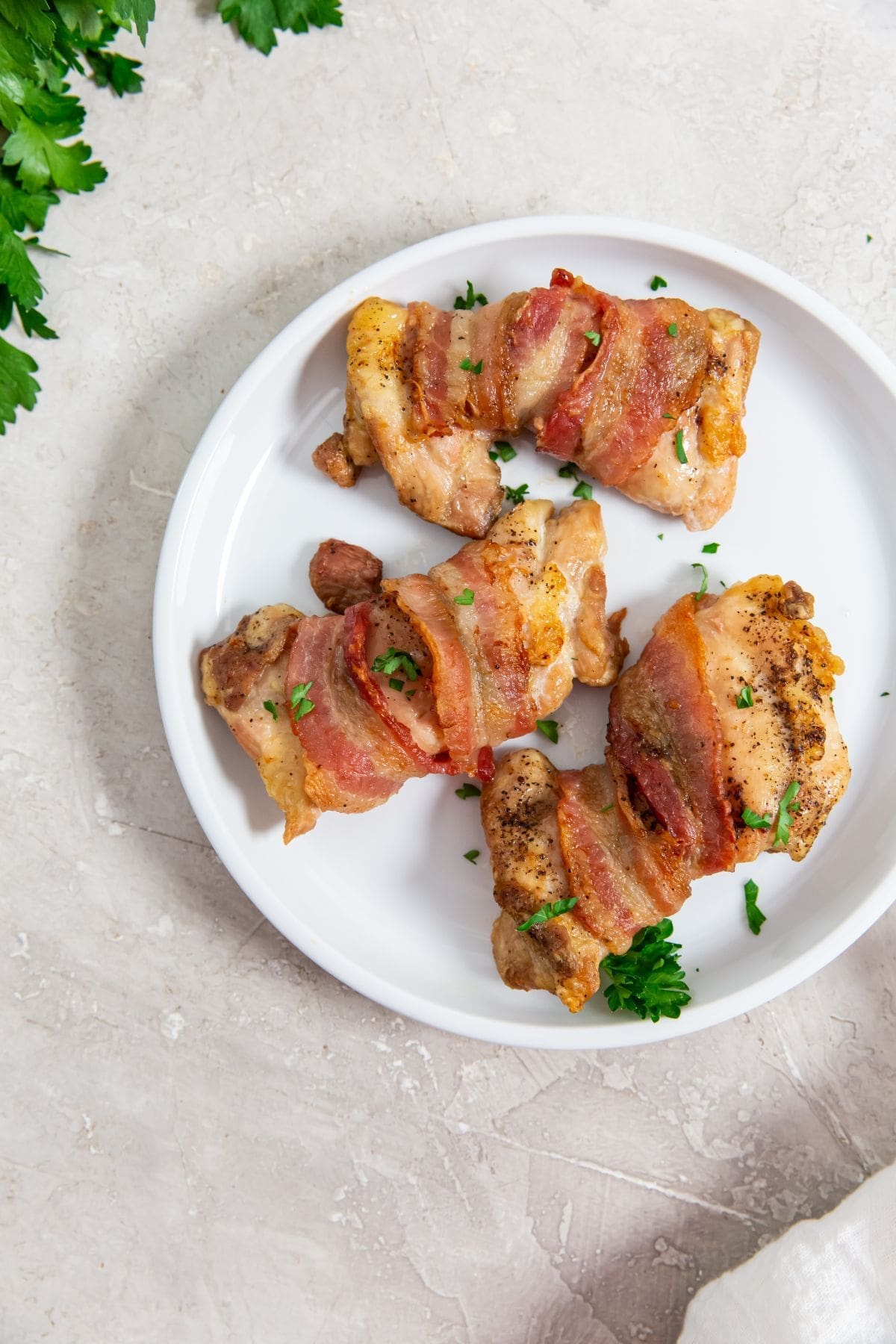 white plate with chicken on it parsley spindled on top. white towel and parsley on top.
