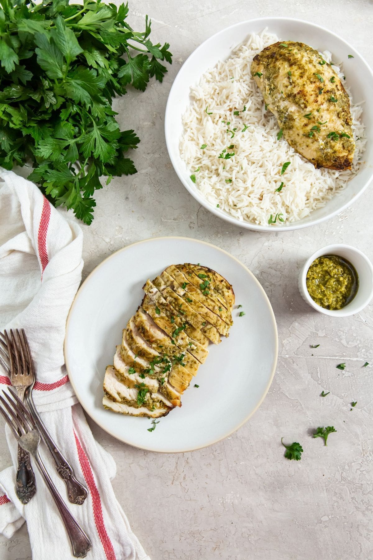 two plates one has just chicken the other has chicken and rice. parsley and pesto in the back.
