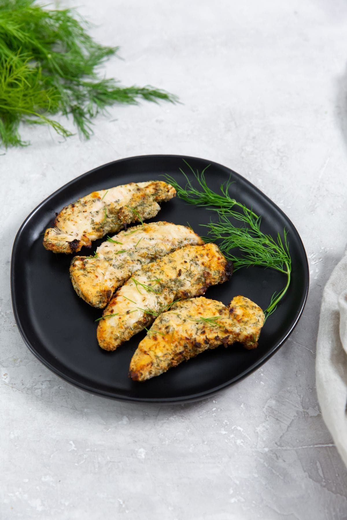 black plate with chicken and dill on it. dill and towel in the back