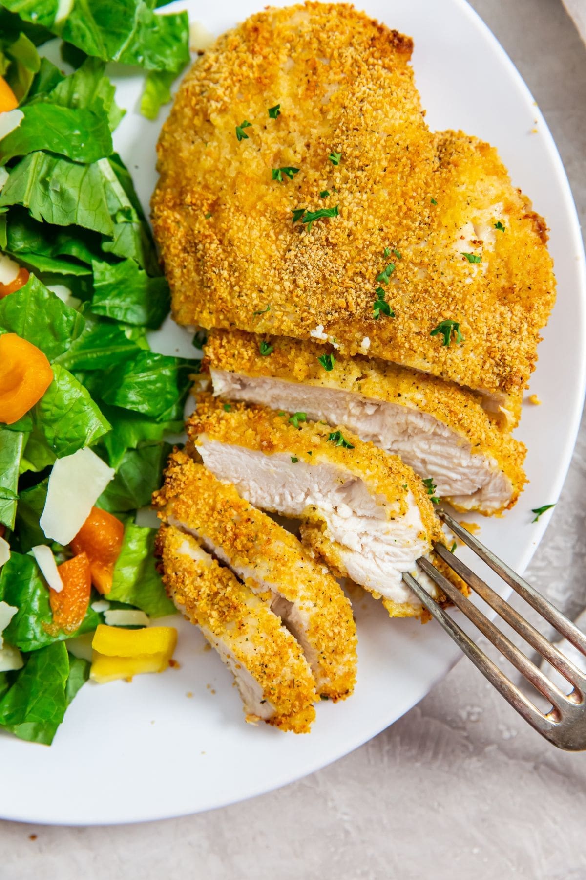 white plate with cut up chicken and salad on plate. fork on plate
