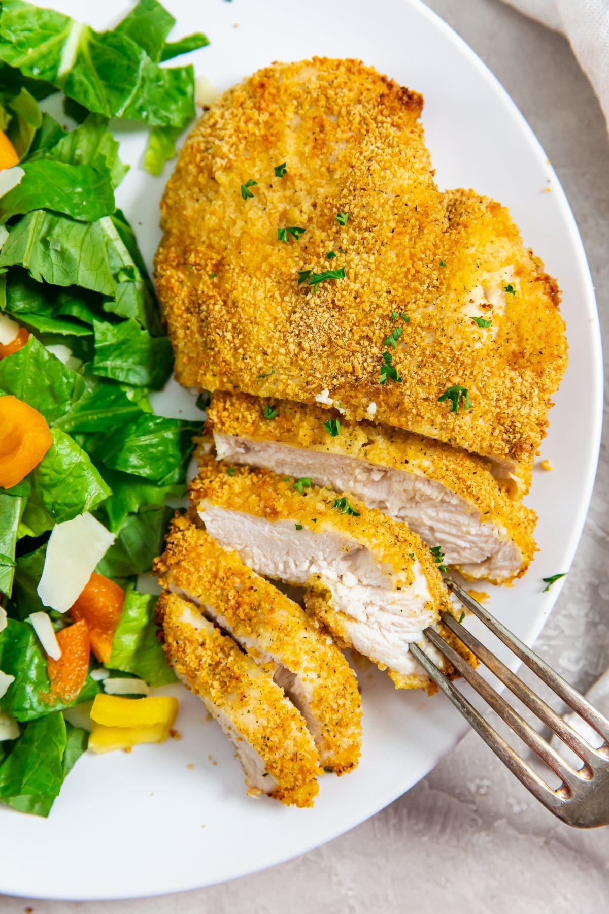 white plate with cut up chicken and salad on plate. fork on plate
