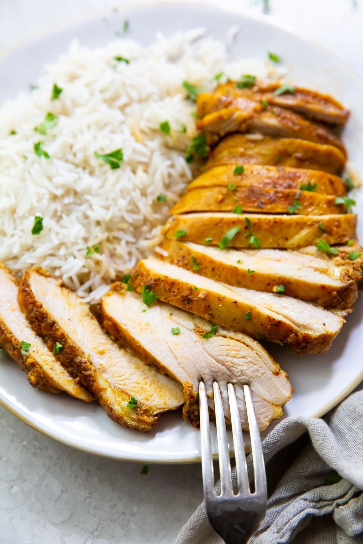 white plate with chicken thighs and rice on it parsley sprinkled on top. Naan on the side gray towel and parsley in the back fork on the plate