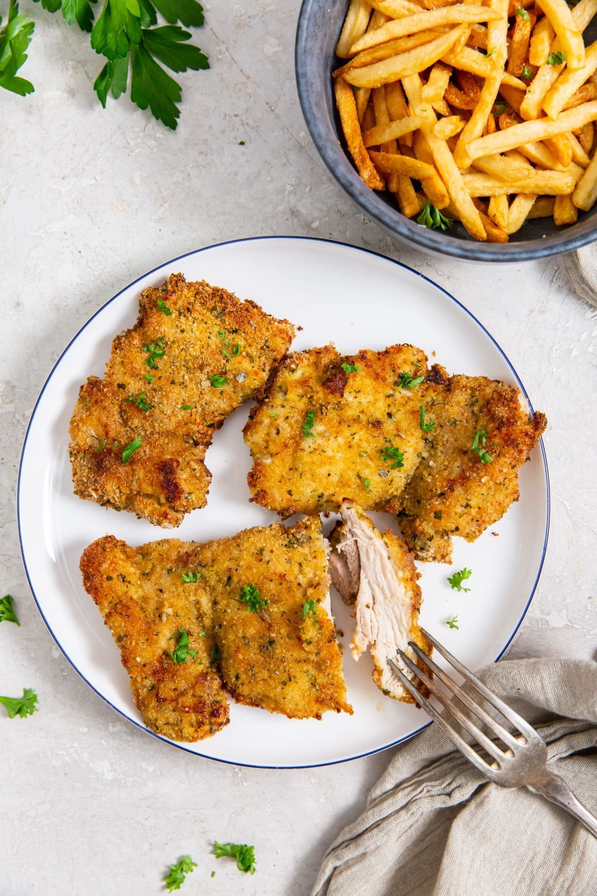 white plate with chicken on it. fries on the side. parsley and towel in the back