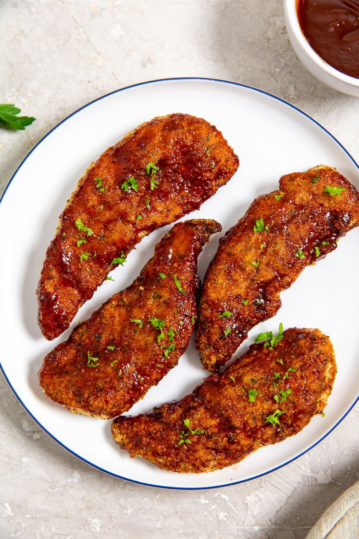 white plate with chicken on it parsley and bbq sauce in the back