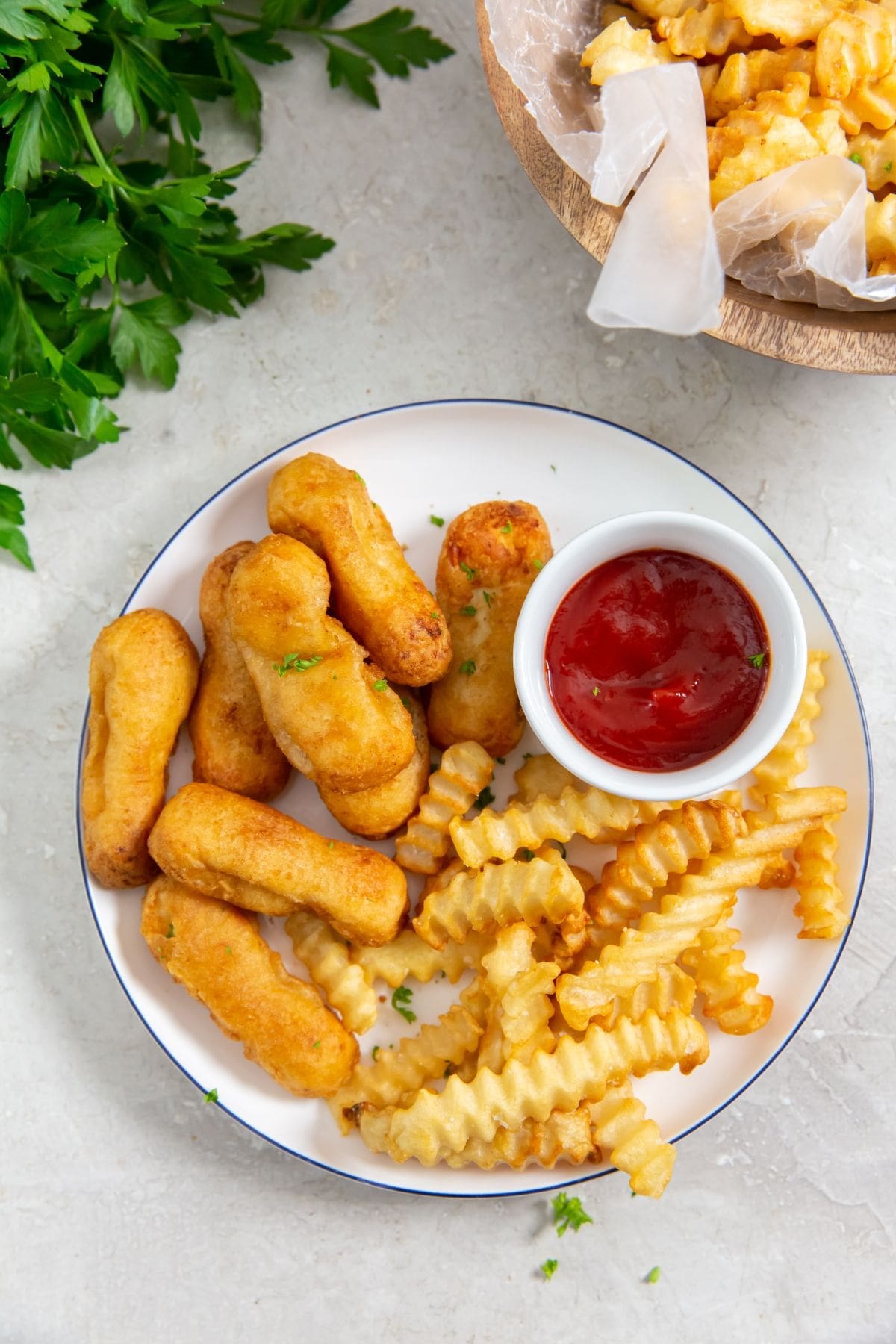 plate with chicken and fries on it parsley in the back with a bowl of fries