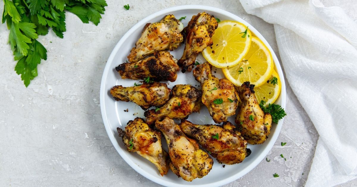 white plate with chicken and lemons on it. parsley in the back.