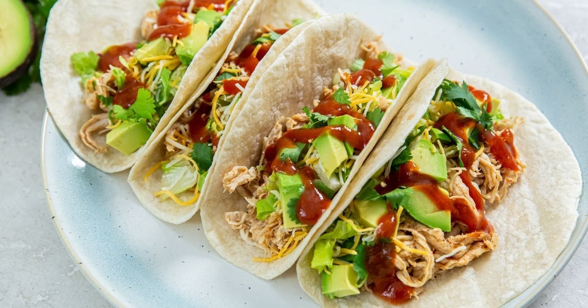 Air Fryer Chicken Tacos on a light blue plate with cheese, avocados, cilantro, and red sauce.