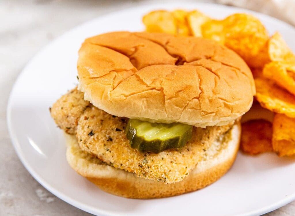 white plate with chicken sandwich and chips on it.