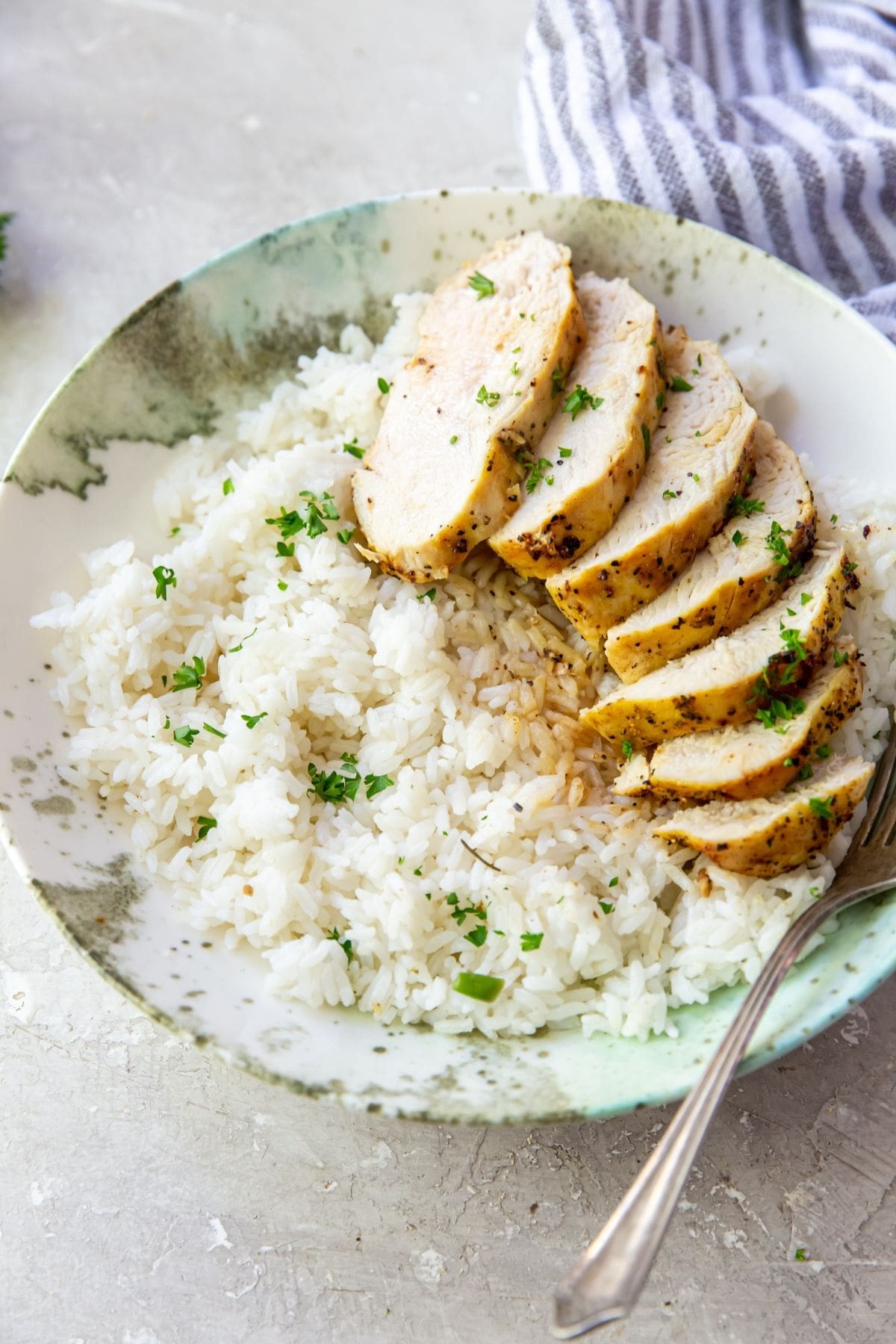 chicken breast on a plate with rice and parsley.